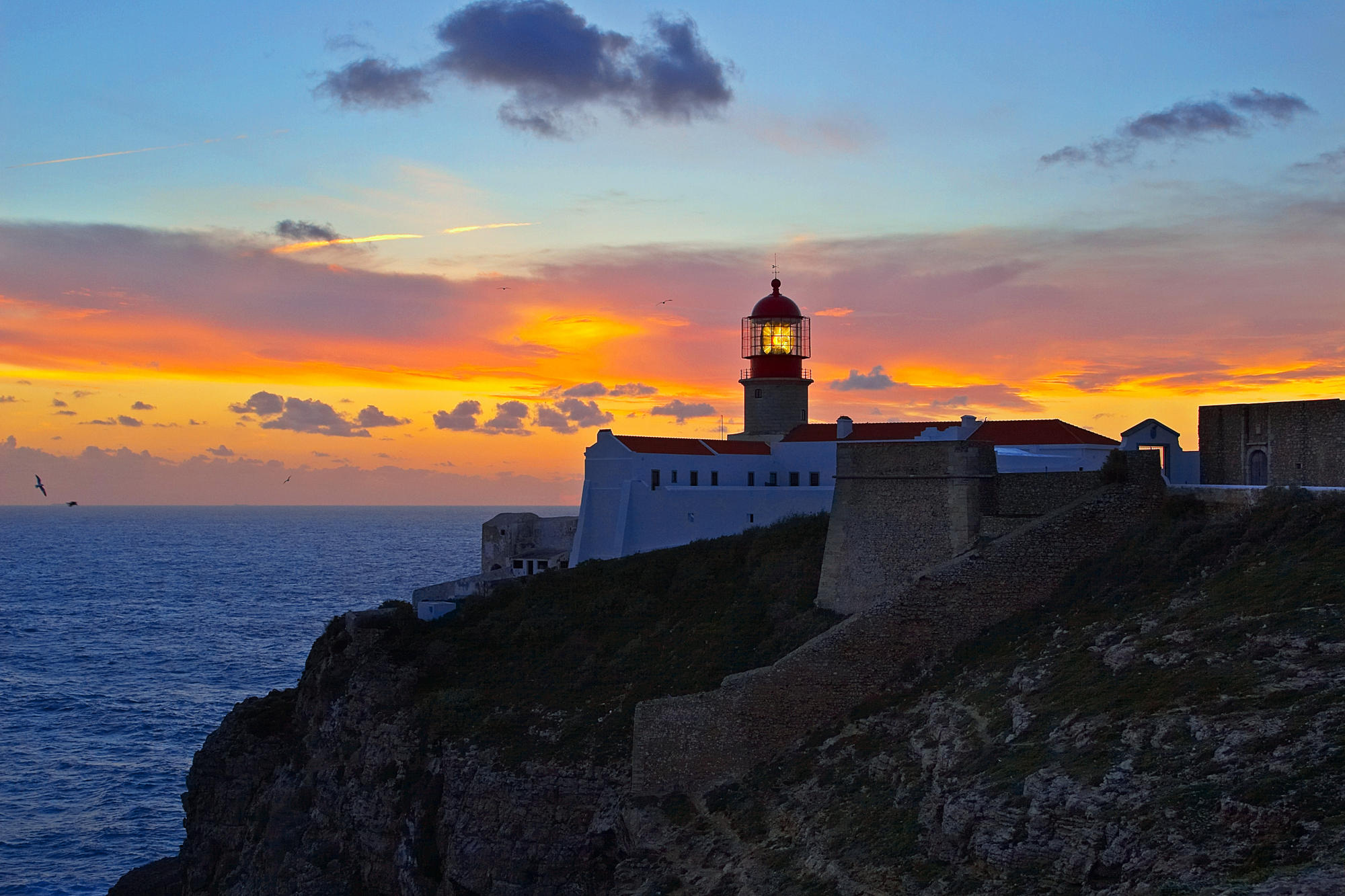 Free download wallpaper Sunset, Sky, Ocean, Cliff, Lighthouse, Cloud, Man Made on your PC desktop