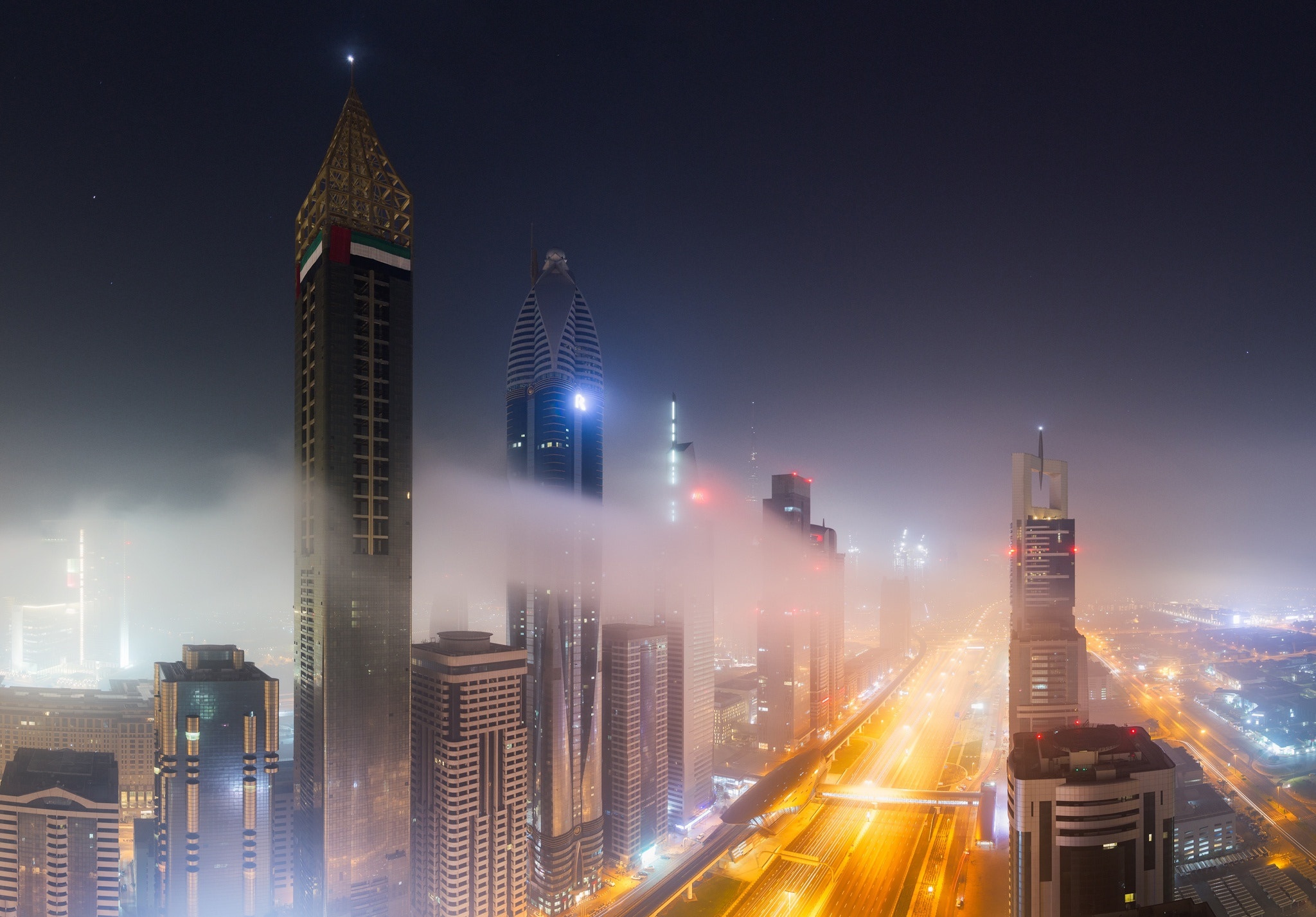 Baixar papel de parede para celular de Cidades, Noite, Arranha Céu, Luz, Dubai, Construção, Rua, Emirados Árabes Unidos, Feito Pelo Homem, Neblina, Aéreo gratuito.