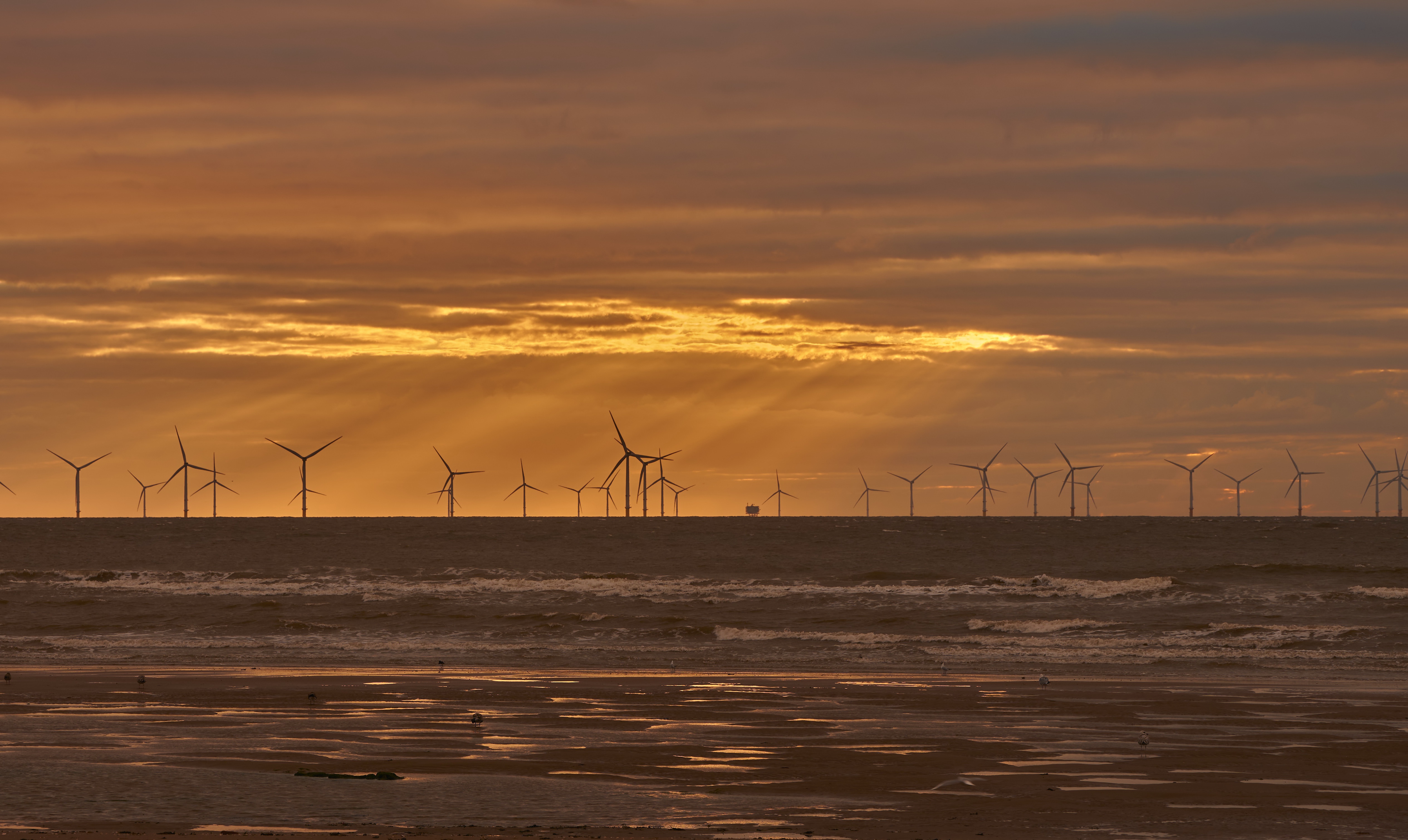 Download mobile wallpaper Sunset, Sea, Horizon, Wind Turbine, Sunbeam, Man Made for free.