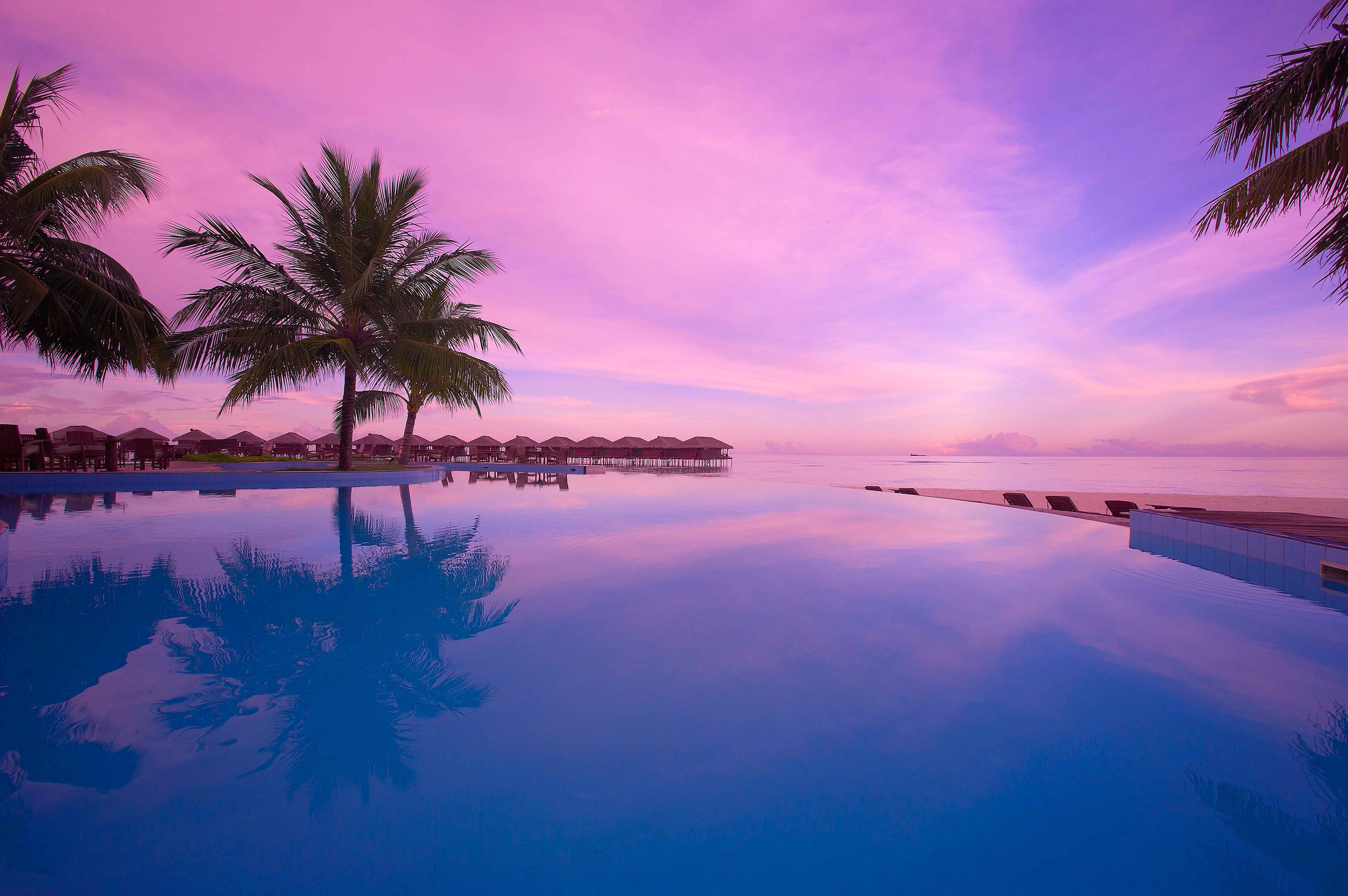 Download mobile wallpaper Sunset, Sky, Pink, Horizon, Purple, Tropical, Resort, Pool, Bungalow, Man Made, Palm Tree for free.