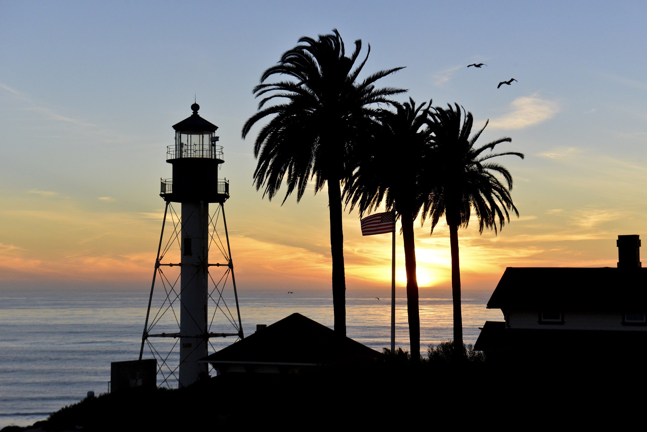 Free download wallpaper Sunset, Usa, Silhouette, Dusk, Evening, Lighthouse, Man Made, American Flag, Palm Tree on your PC desktop