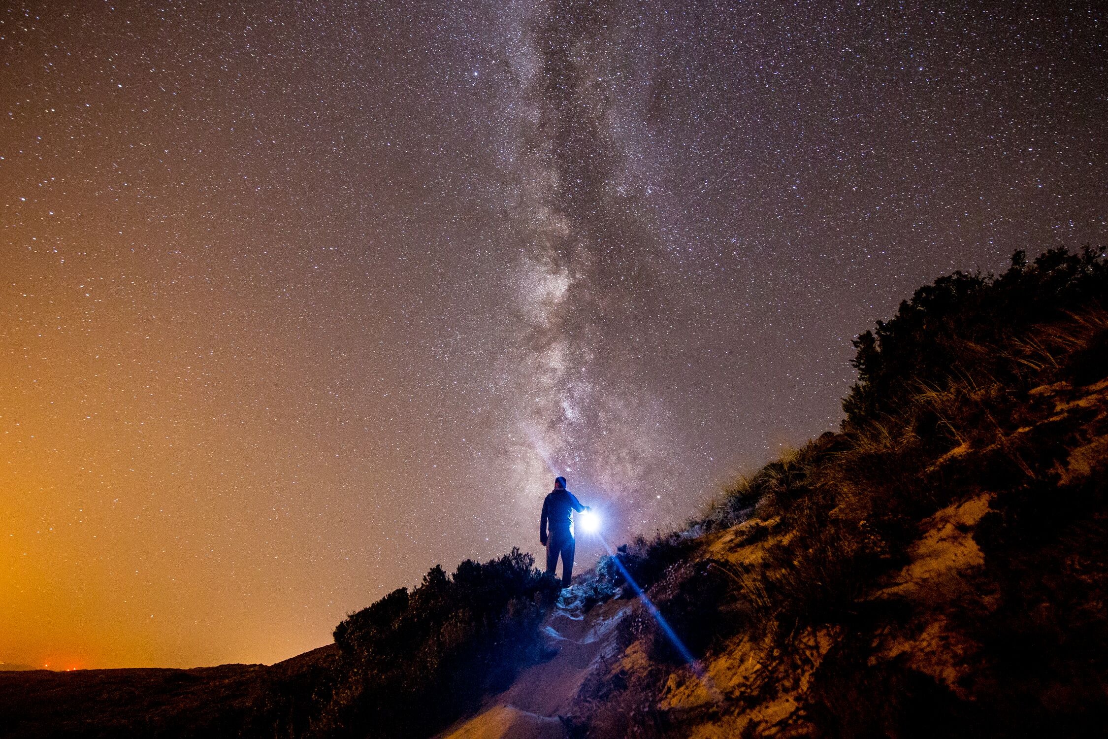 Download mobile wallpaper Person, Starry Sky, Mountains, Nature, Shine, Human, Light for free.