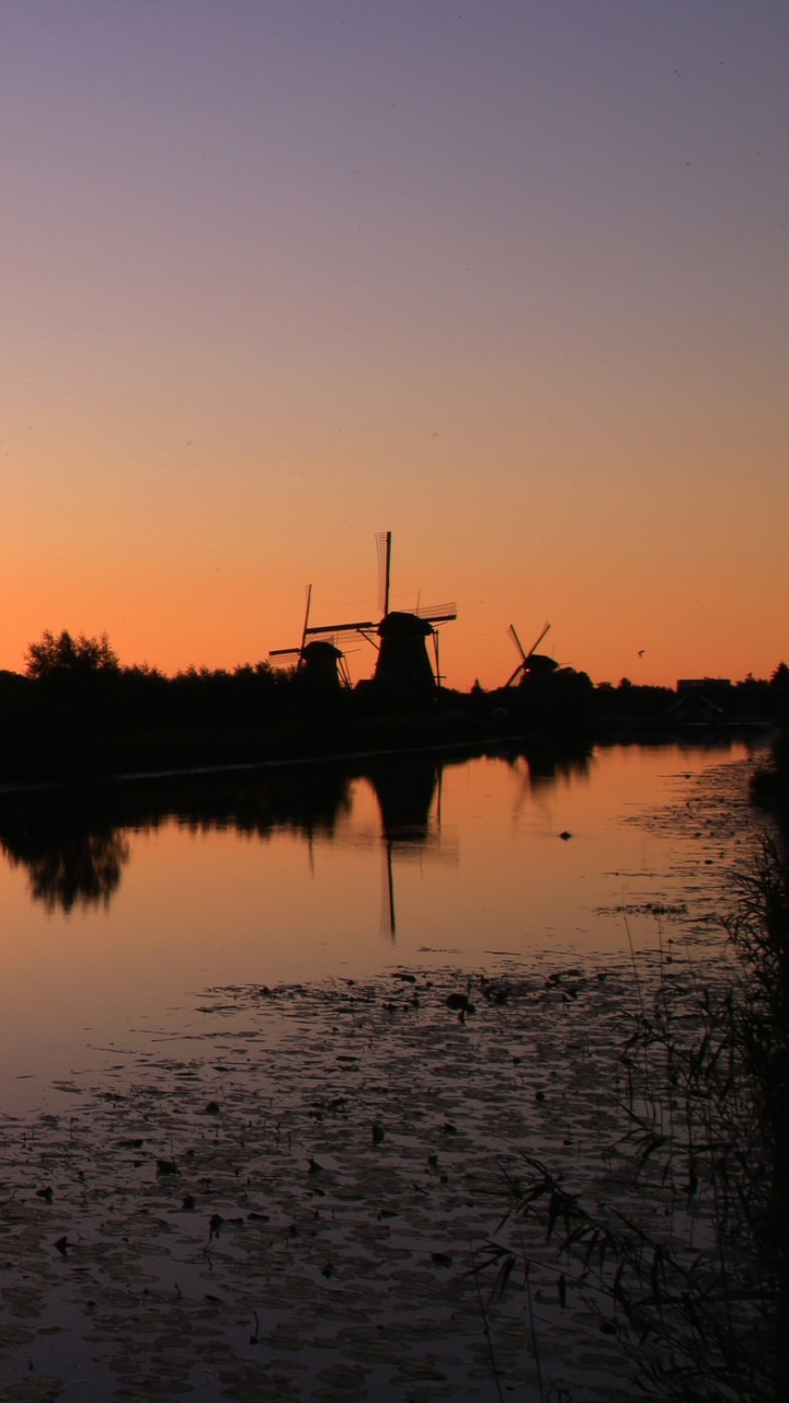Download mobile wallpaper Sunset, Building, Silhouette, River, Windmill, Man Made for free.