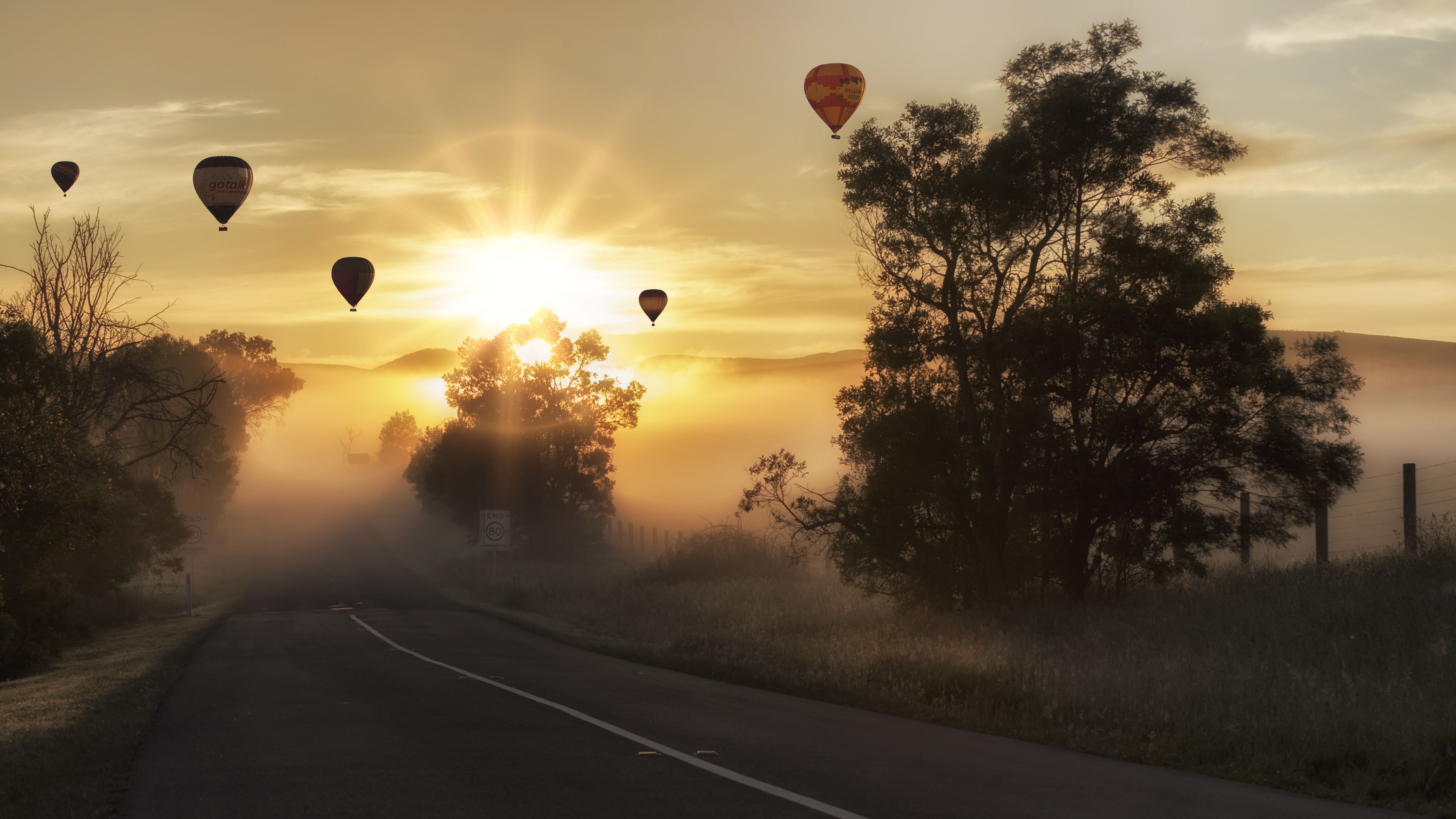 Download mobile wallpaper Landscape, Sun, Road, Tree, Fog, Sunrise, Photography, Vehicle, Sunbeam, Hot Air Balloon for free.