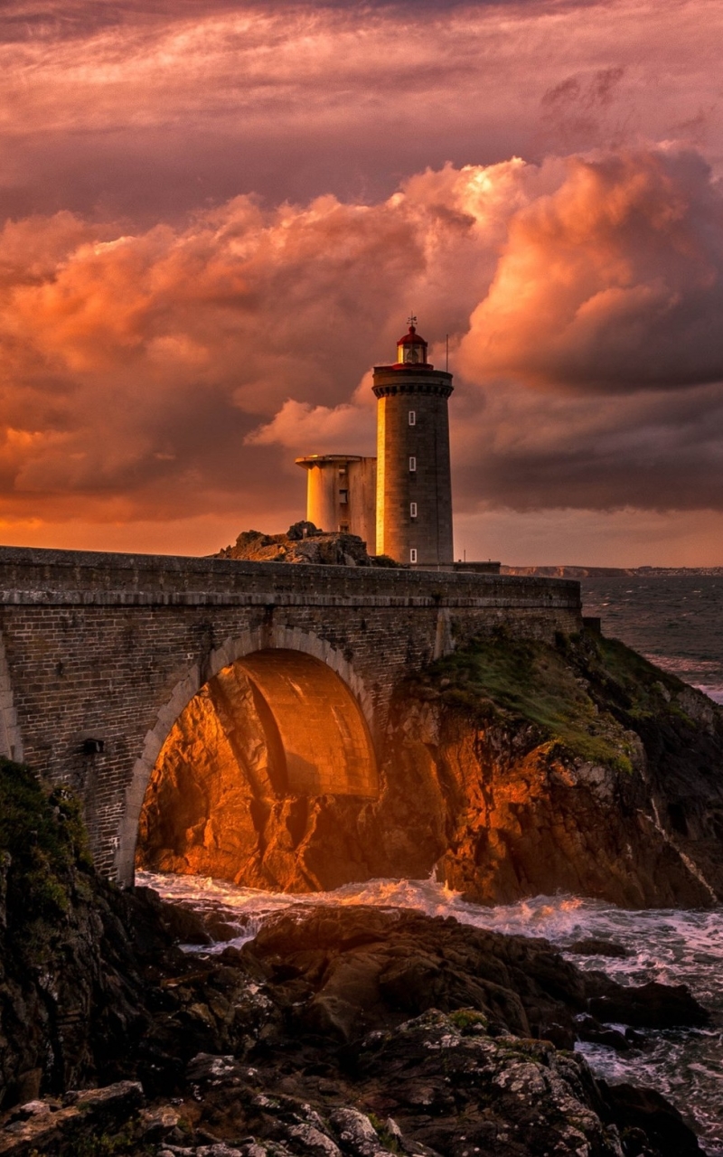 Download mobile wallpaper Sunset, Sky, Bridge, Evening, Lighthouse, Arch, Cloud, Man Made for free.