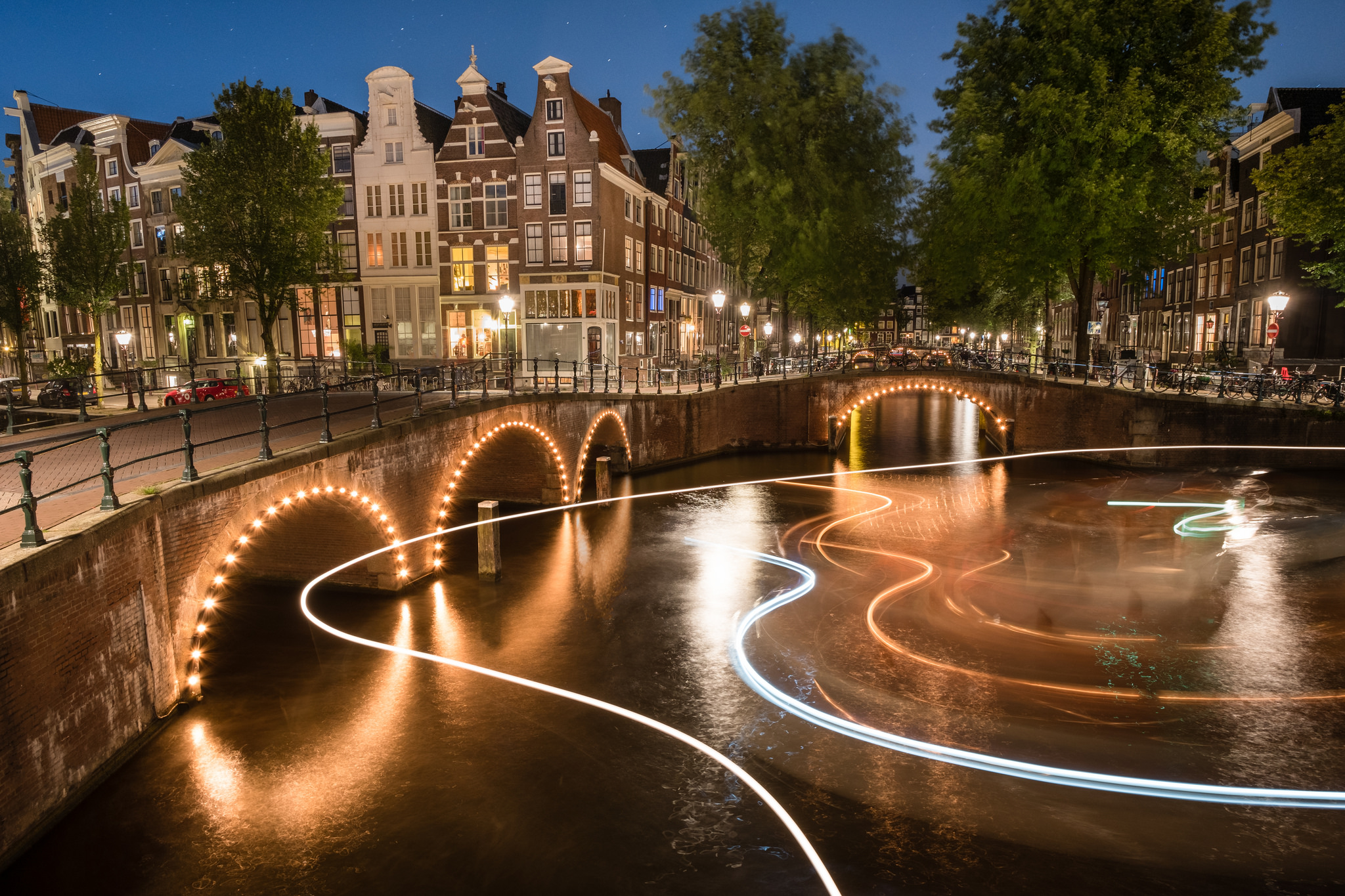 Скачать картинку Города, Ночь, Город, Свет, Нидерланды, Амстердам, Сделано Человеком, Замедленная Киносъёмка в телефон бесплатно.