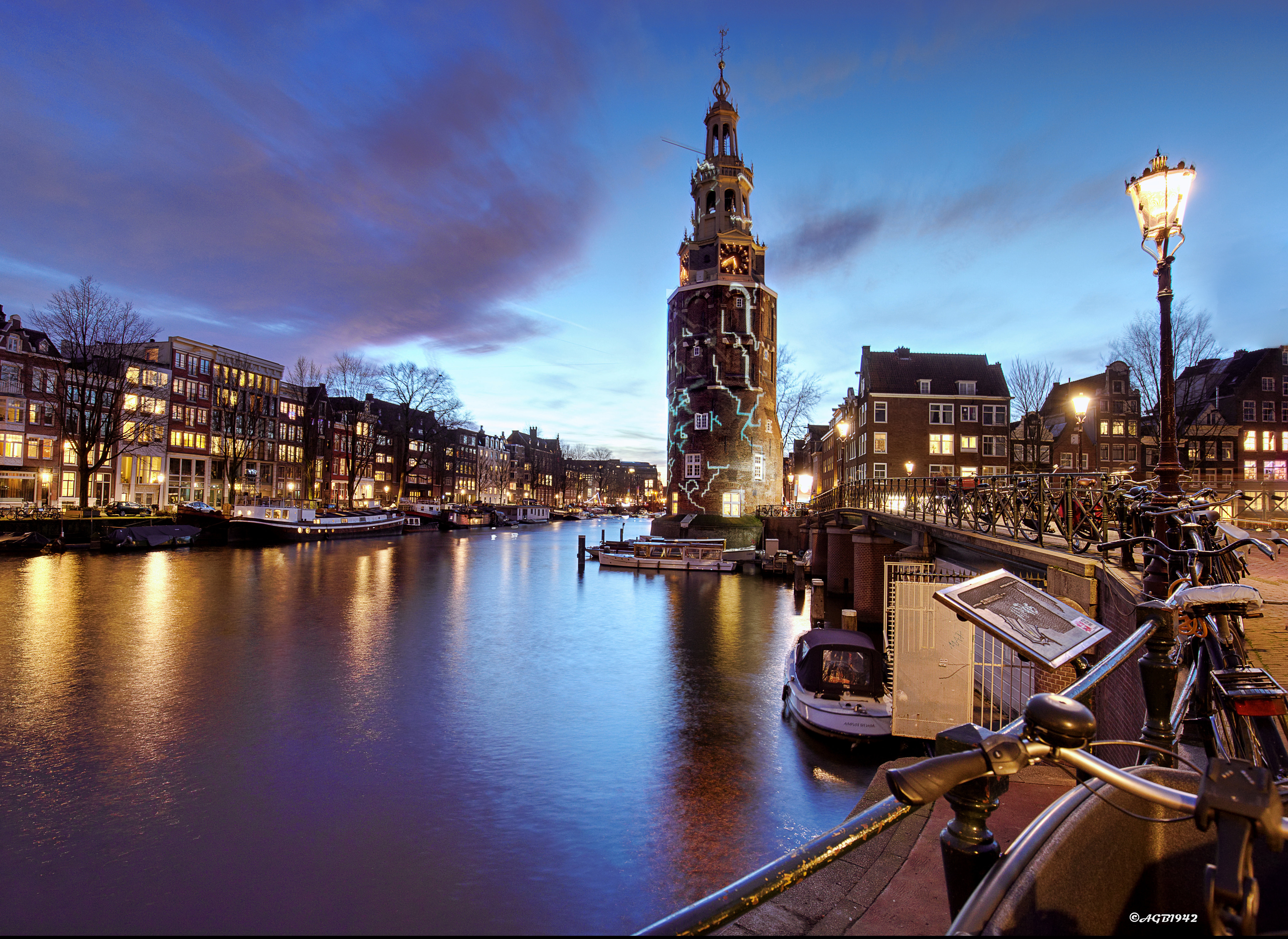 Скачать картинку Города, Город, Дом, Вечер, Лодка, Здание, Башня, Нидерланды, Канал, Амстердам, Сделано Человеком в телефон бесплатно.