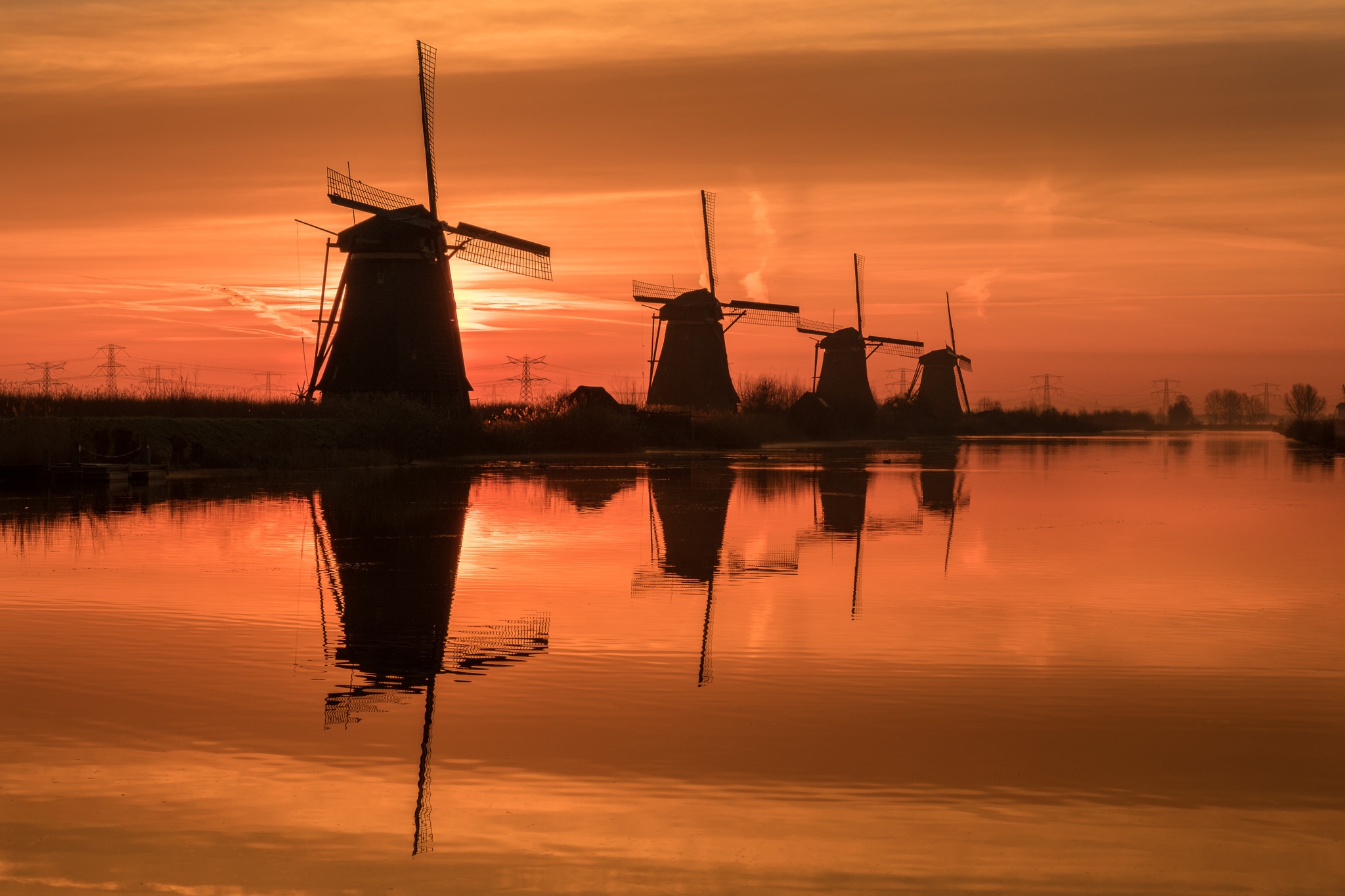 Download mobile wallpaper Sunset, Reflection, Silhouette, River, Windmill, Man Made, Orange (Color) for free.