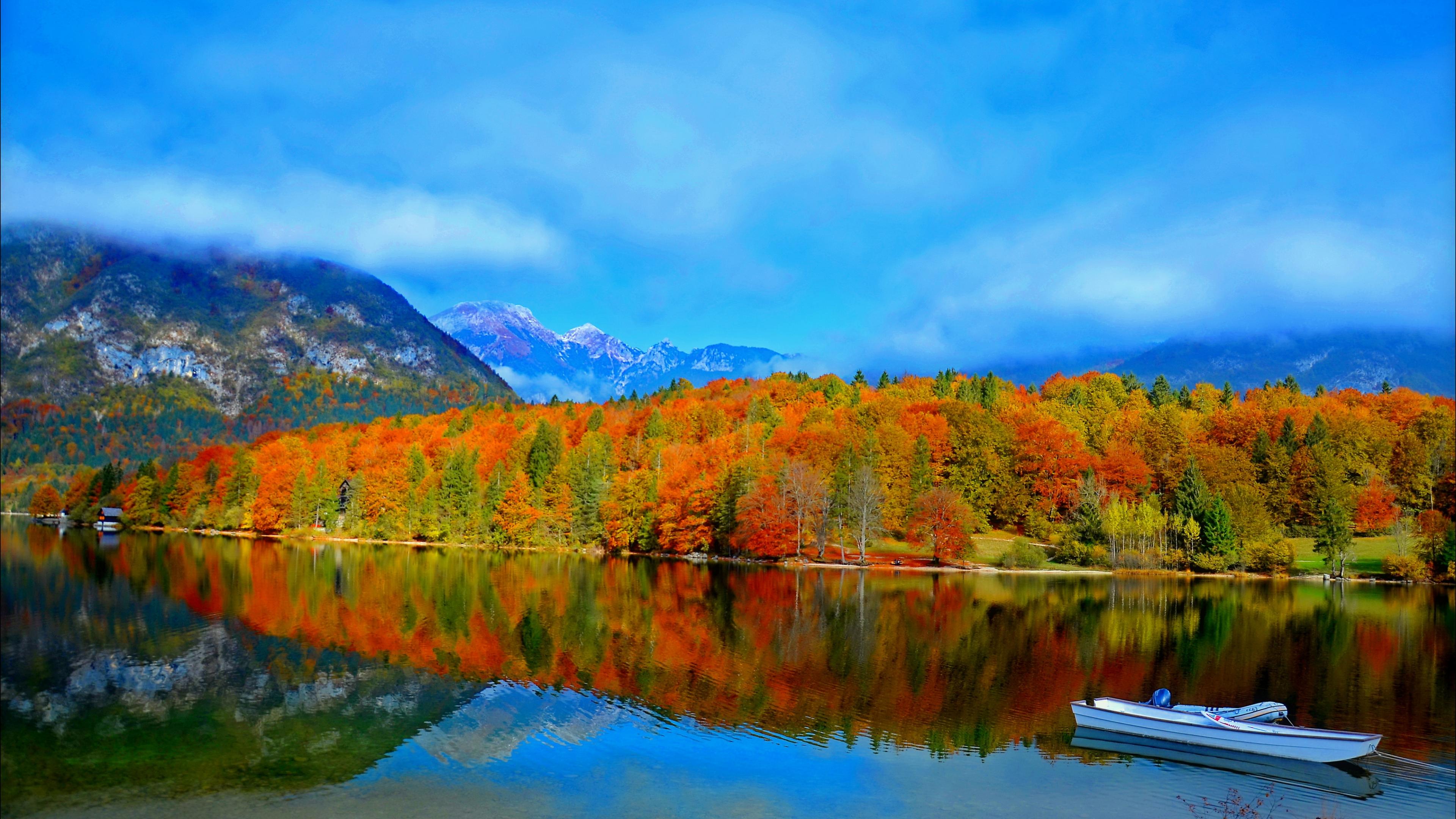 Скачать картинку Осень, Облака, Гора, Озеро, Отражение, Лес, Дерево, Земля, Лодка, Фотографии в телефон бесплатно.
