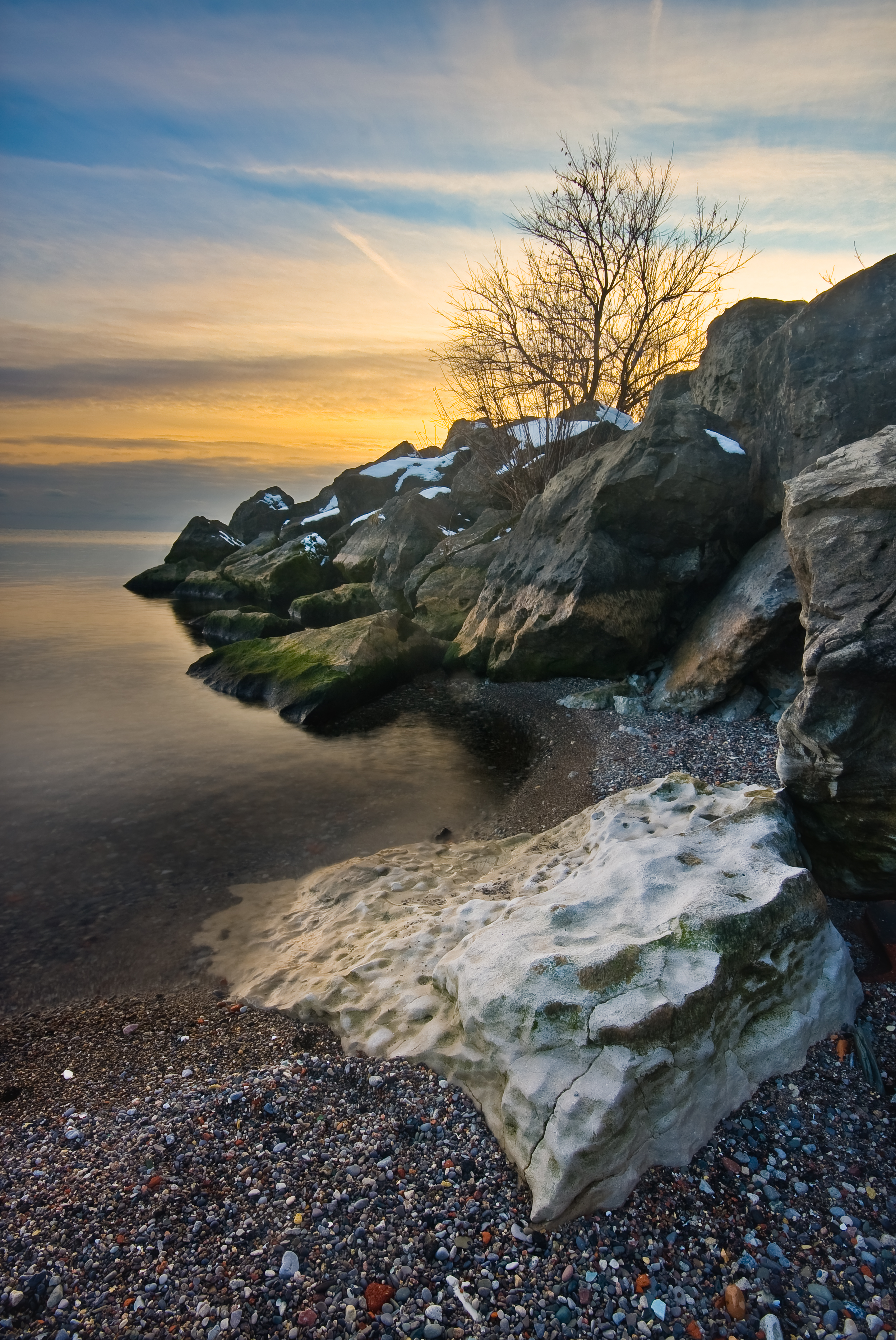 Download mobile wallpaper Shore, Bank, Tree, Rocks, Wood, Nature, Sunset, Sea, Landscape for free.